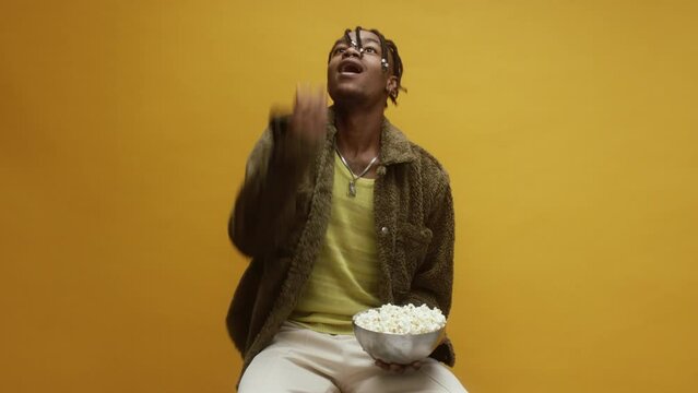 A young black man is throwing popcorn into his mouth 
