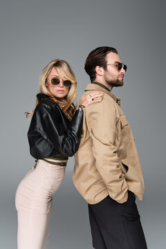 stylish blonde woman in sunglasses leaning on shoulders on bearded man isolated on grey