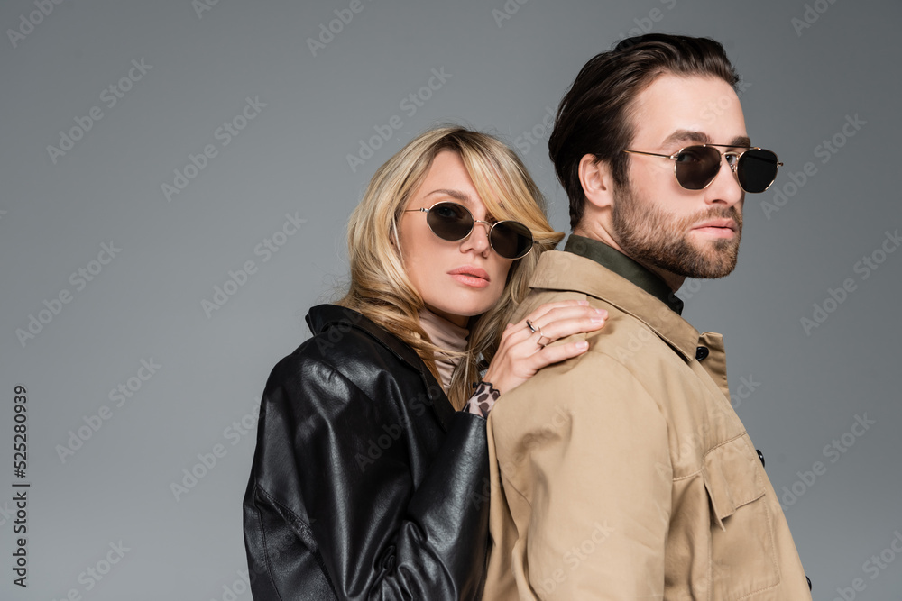 Wall mural stylish blonde woman in sunglasses and leather jacket leaning on shoulders on bearded man isolated o