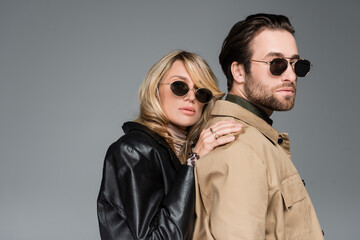 stylish blonde woman in sunglasses and leather jacket leaning on shoulders on bearded man isolated...