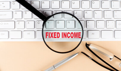 Text FIXED INCOME on keyboard with magnifier , glasses and pen on beige background