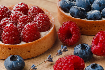 Sweet tarts with fresh raspberries and blueberries on wooden background. Freshly homemade fruit cake, summer berries and sprigs of lavender on a table. macro photography very close up