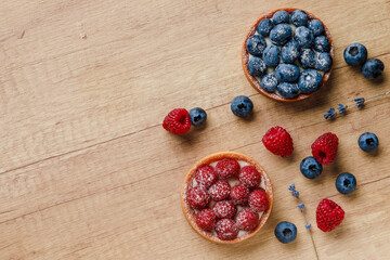 Sweet tarts with fresh raspberries and blueberries on wooden background. Freshly homemade fruit cake, summer berries and sprigs of lavender on a table. Top view Place for text