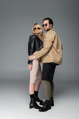 full length of stylish man in autumnal outfit and sunglasses posing with woman on grey