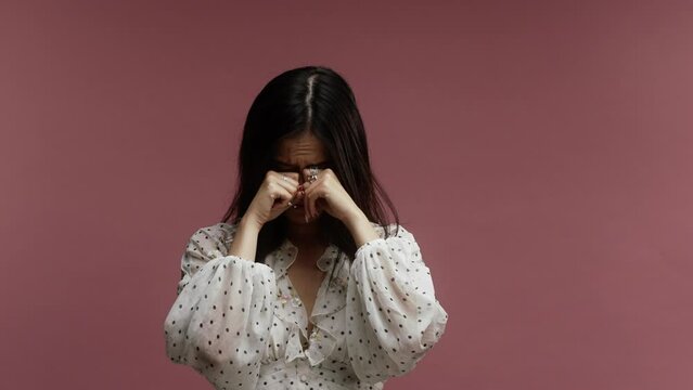 A young asian woman on a pink background crying 