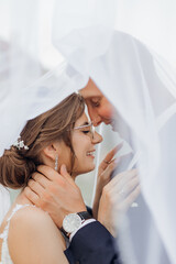 Closeup vertical portrait of smiling, chancy married couple of young woman in glossy dress and groom covered by veil