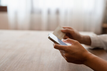 Close up female hands holding credit card and smartphone, young woman paying online, using banking service, entering information, shopping, ordering in internet store, doing secure payment