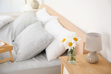Bouquet of beautiful daisy flowers and lamp on nightstand in bedroom, space for text