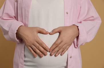 Pregnant woman on light brown background, closeup