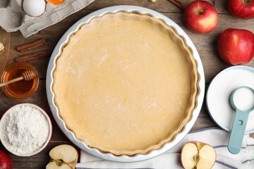 Raw dough and ingredients for traditional English apple pie on wooden table, flat lay