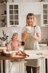 young woman in chef's apron and her little son are preparing apple pie at home in cozy kitchen