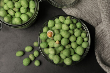 Tasty wasabi coated peanuts on black table, flat lay