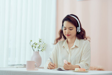 Naklejka premium Woman with headphones and a diary eating macarons in living room