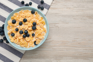 Bowl of tasty crispy corn flakes with milk and blueberries on wooden table, flat lay. Space for text