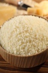 Bowl with grated parmesan cheese on wooden table, closeup