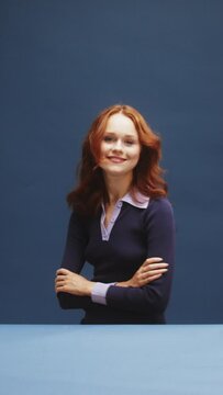 A white ginger woman on a blue background is turning around and winking 