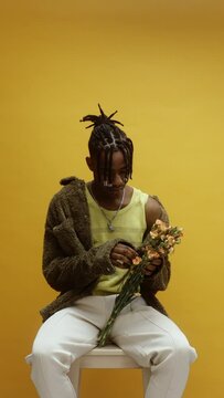 A young black man pulling out flower petals on a yellow background 