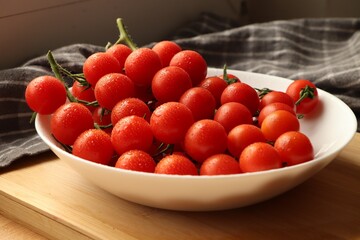 Plate of ripe whole cherry tomatoes with water drops on wooden table, closeup