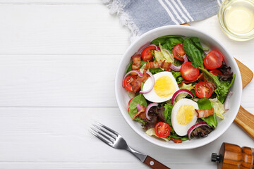Delicious salad with boiled egg, bacon and vegetables served on white wooden table, flat lay. Space...