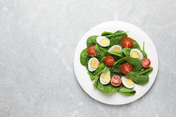 Delicious salad with boiled eggs, tomatoes and spinach on light grey table, top view. Space for text