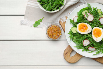 Delicious salad with boiled egg, vegetables and arugula served on white wooden table, flat lay. Space for text