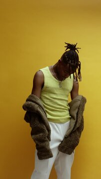 A young black man on a yellow background standing proudly and looking at the camera
