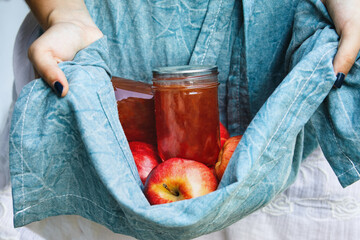 Woman's hands holding out apron filled with fresh gala apples and homemade apple jelly. Selective...