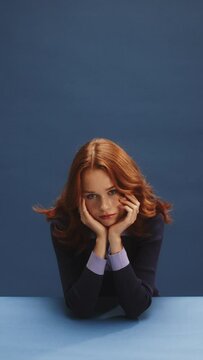 A whit ginger girl on a blue background looking confidently at the camera and waiting 