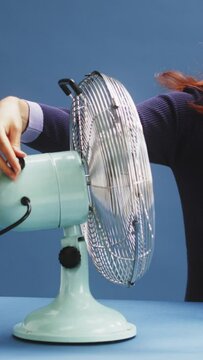 a young white ginger woman on a blue background being hot and turning on the fan