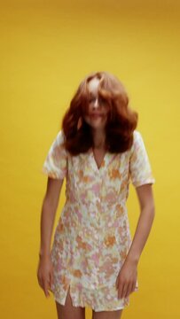 A young white ginger woman appearing on a yellow background waving to the camera