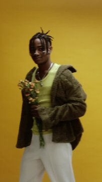 A young black man on a yellow background sniffing bouquet of flowers  