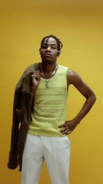A young black man on a yellow background standing proudly and looking at the camera