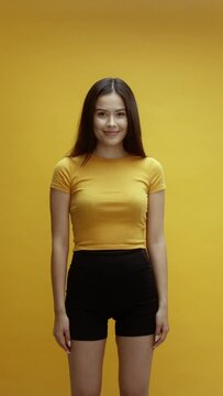 A young asian woman on a yellow background is being playful covering her eyes and smiling