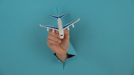 A female hand sticking out of a hole from a blue background holds a model of an airplane. 