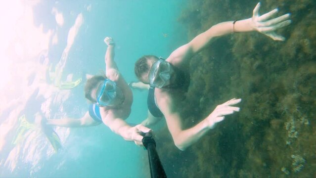 two male friends swim with masks and snorkels underwater in the sea among algae, selfie of happy tourists, snorkeling