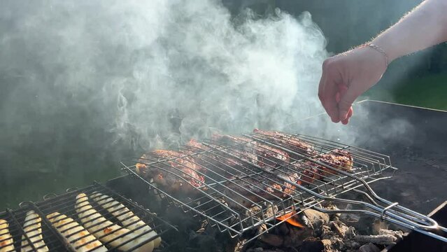 Bbq meat on a grill grate. Man sprinkles salt on meat. Picnic time
