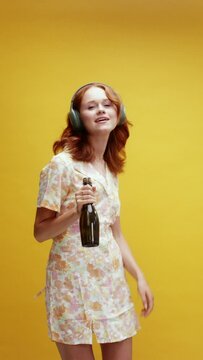 A young ginger white woman wearing headphones dancing with a bottle of champagne 
