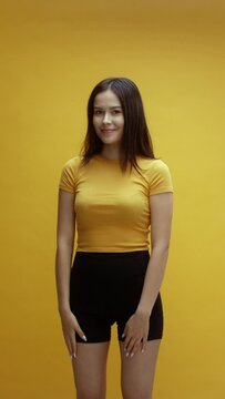 A young Asian woman being cute and walking off camera, in front of a yellow background