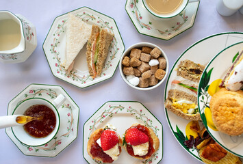 Delicious British Afternoon Tea Table with White China Cups, Tea, Scones with Jam Cream,...