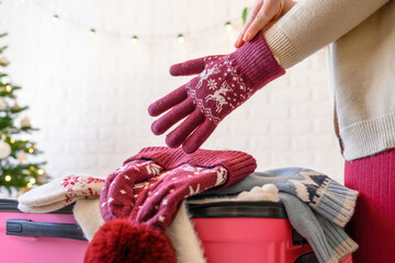 Christmas time. Woman putting knitted winter clothing in a suitcase in the room decorated christmas...