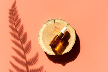 Amber glass dropper bottle on woodcut in the sunlight with eucalyptus flower shadows. Top view. Luxury and natural cosmetics presentation. Testers, beauty samples perfumery concept. Shades and lights