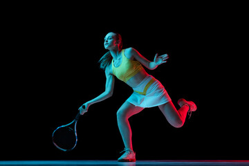 Young woman, professional tennis player training isolated on blue background in neon.