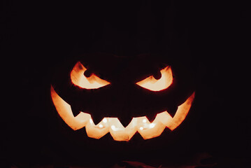 Spooky smile and sinister eyes of the pumpkin in the darkness. Illuminated face of jack-o-lantern isolated on black background