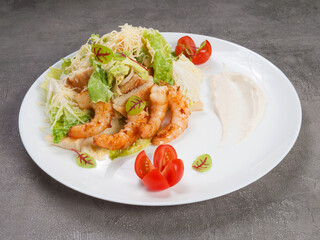 caesar salad with shrimp on a white plate on a gray background