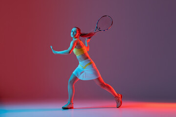 Full length portrait of young woman playing tennis isolated on dark background in neon. Healthy lifestyle, fitness, sport, exercise concept.