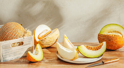 Various sliced melons on wooden table by stone wall