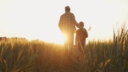 Farmer and his son in front of a sunset agricultural landscape. Man and a boy in a countryside field. Fatherhood, country life, farming and country lifestyle. © Acronym