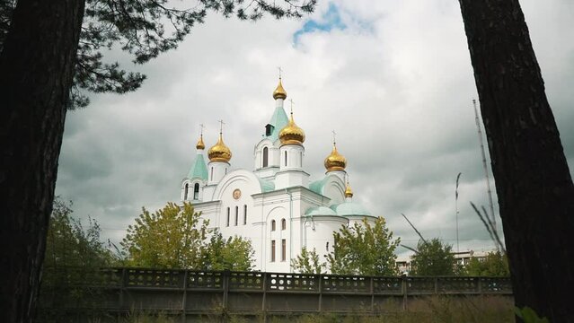Christian cathedral with golden domes and crosses against skies. Church in the woods zoom out panorama. Distant monastery - heaven with clouds. Religion and faith.