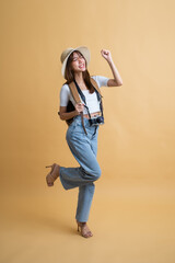 Full length of young attractive Asian woman traveler in casual clothes wearing straw hat with backpack and camera isolated on yellow background, Tourist girl having cheerful holiday trip concept