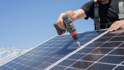 Solar panel technician with drill installing solar panels on roof. technician installing...